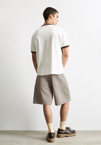 T-shirt blanc avec des bordures sombres, shorts gris, chaussettes claires et chaussures à plateforme marron. Les shorts comportent deux poches arrière.