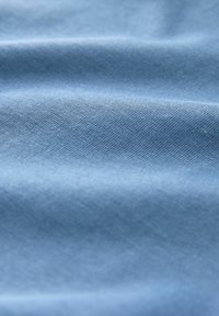 Material moale, albastru deschis, cu pliuri delicate și textură fin țesută vizibilă la vedere apropiată.