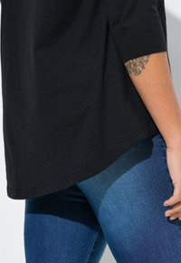 Haut noir à manches courtes avec une coupe décontractée, associé à un jean en denim bleu. Le jean présente un dégradé plus clair sur la jambe.