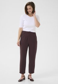 Bordeaux højtaljede bukser med sidelommer, plisseret front og tapered ben-design, parret med en tætsiddende hvid kortærmet top.