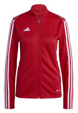 Veste zippée rouge en tissu lisse avec des rayures blanches le long des manches et un col haut. Un logo est également présent sur la poitrine.