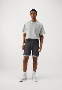 Camiseta de algodón gris, de manga corta; pantalones cortos de mezclilla oscura con dobladillos enrollados; zapatillas altas azul claro; fondo liso.