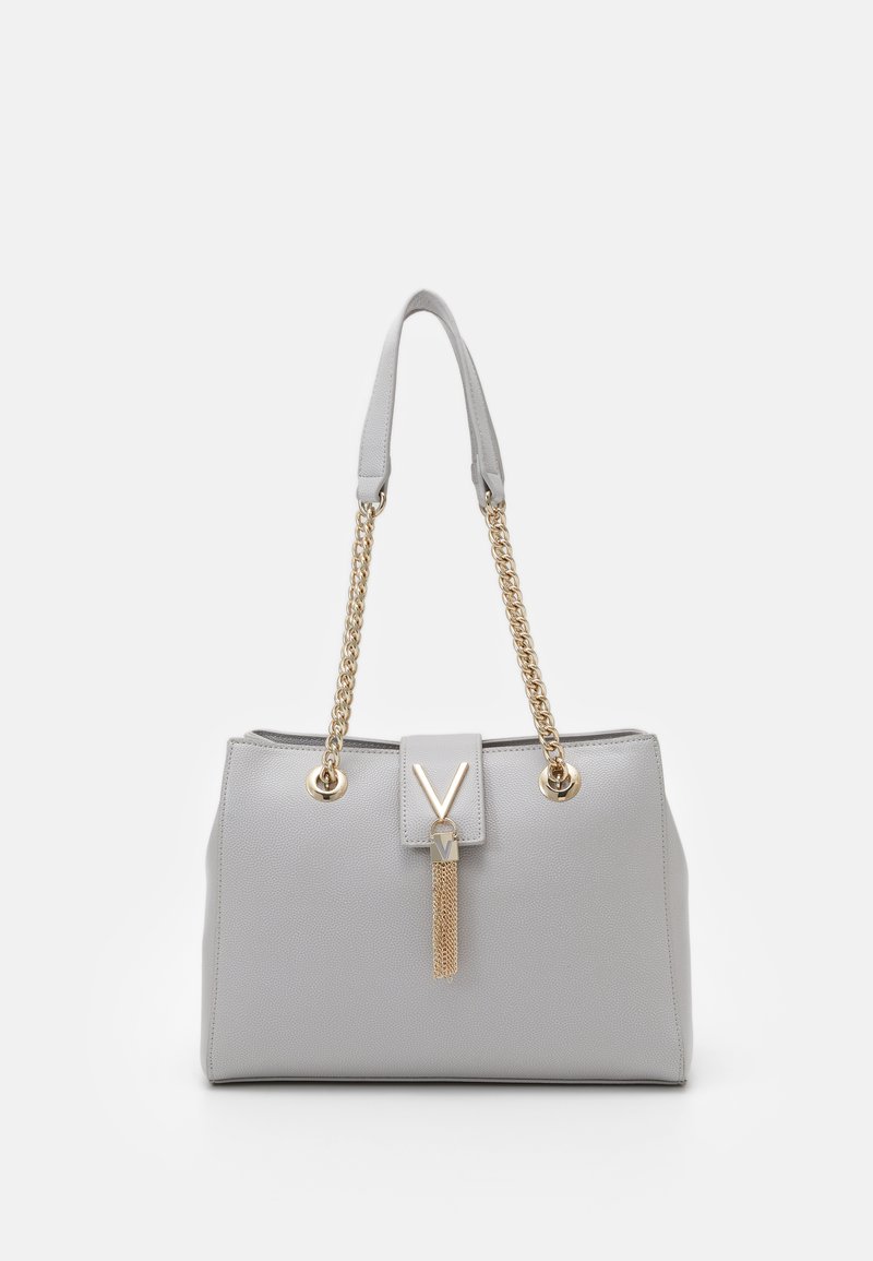 Bolsa de couro cinza com forma estruturada, alças de corrente douradas e um pompom decorativo. Apresenta um logótipo em destaque em forma de "V" na frente.