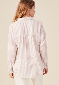 Camicia a maniche lunghe a righe rosa chiaro, con colletto, dettagli plissettati sul retro e orlo curvo. Il tessuto sembra morbido e testurizzato.