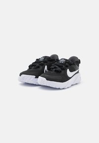 Chaussures de sport noires avec une texture striée, des accents blancs et un col rembourré. Possède un logo swoosh blanc et une semelle blanche texturée.