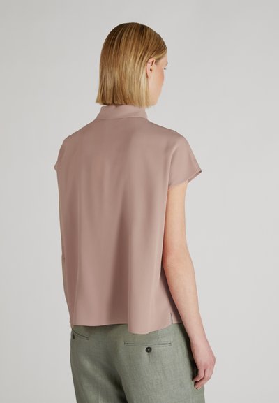 Top rosa chiaro a maniche corte con una vestibilità larga, caratterizzato da un colletto alto e una texture liscia. Abbinato a pantaloni verde chiaro con tasche posteriori.