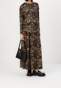 Top en rok met luipaardprint gemaakt van zacht tissu; zwarte handtas en stevige zwarte schoenen maken de outfit compleet.