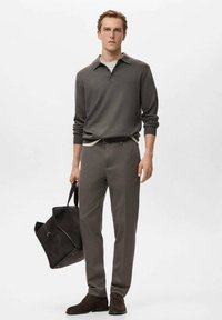 Maglione grigio con colletto, indossato sopra una camicia più chiara, abbinato a pantaloni su misura coordinati. Porta una borsa scamosciata scura e indossa scarpe scure.