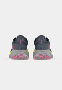 Grijze sportieve schoenen met roze accenten en gele zolen. Bevat een gestructureerd bovenwerk en een gevoerde, contourede buitenzool voor ondersteuning.
