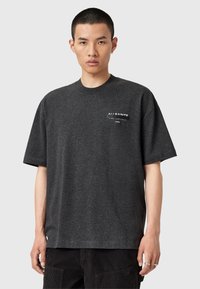 T-shirt noir à manches courtes avec un col rond et un petit imprimé graphique blanc sur la poitrine gauche. Fabriqué en tissu doux et texturé.