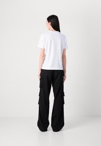 Camiseta blanca de algodón con mangas cortas, combinada con pantalones cargo negros de pierna ancha que tienen múltiples bolsillos laterales y un ajuste relajado.