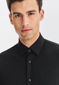 Czarna koszula na guziki z klasycznym kołnierzykiem, charakteryzująca się gładką fakturą i subtelnym połyskiem. Posiada zapięcie na guziki i wyraźnie zarysowane ramiona.