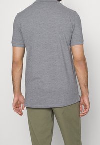 Szary, krótki rękaw polo z miękkiego materiału, z kołnierzykiem i prostym dołem, noszony z khaki spodniami.