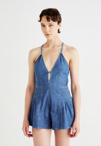Denim jumpsuit met een diepe V-hals, verstelbare bandjes en een keyhole-detail. Heeft een aansluitend lijfje en vloeiende shorts met zichtbare stiksels.