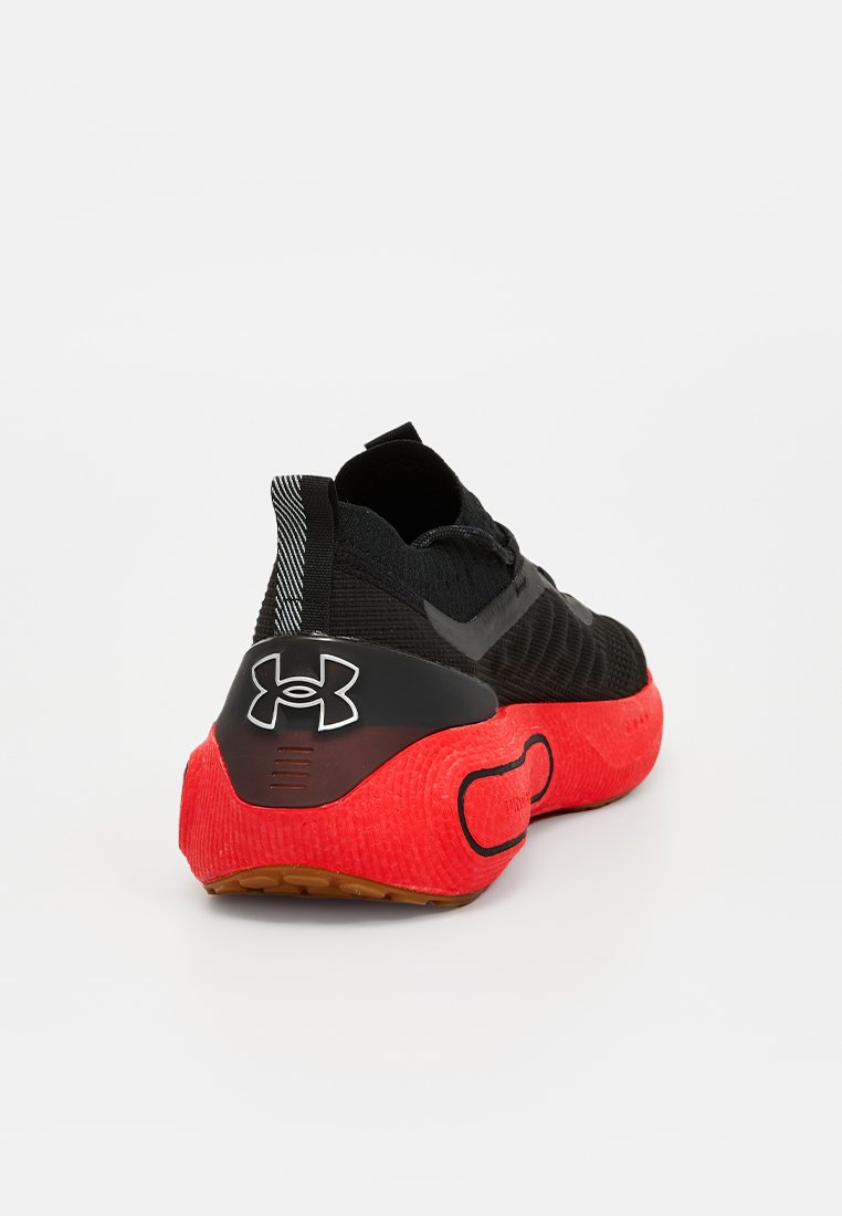 Scarpa sportiva nera con tomaia testurizzata e suola in gomma rossa. Presenta un logo prominente sul tallone e una linguetta a strisce sul retro.