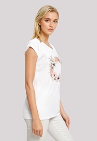 White short-sleeve t-shirt featuring a floral wreath design in colors including pink and green. Soft cotton material with a relaxed fit.