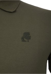 Olivgrünes Poloshirt aus weichem Stoff mit einem dezenten, gestickten schwarzen Logo auf der linken Brust und einem klassischen Kragendesign.
