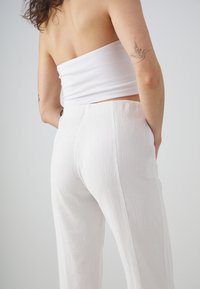 Biela textúrovaná crop top a nohavice s vysokým pásom a širokými nohavicami, obidve s jemným, pokrčeným vzhľadom, na svetlošedom pozadí.