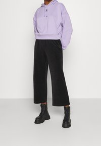 Lavendel beschnittene Kapuzenjacke mit Kordelzugdetail, kombiniert mit schwarzen Cord-weitbeinigen Hosen und klobigen schwarzen Schnürstiefeln.