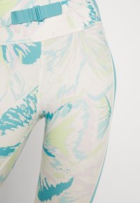 Legginsy w kwiatowy wzór w białym, jasnoniebieskim i turkusowym kolorze. Wykonane z miękkiego, elastycznego materiału, z niebieskim, regulowanym pasem w talii.
