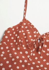 Rustin värinen mekko, jossa on valkoisia pilkkuja, ohutolkaimilla, röyhelökaula-aukolla ja solmukiinnityksellä rinnassa. Pehmeä teksturoitu kangas.