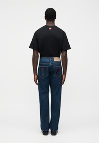 Μαύρο μπλουζάκι με στρογγυλή λαιμόκοψη, συνδυασμένο με μπλε τζιν παντελόνι με τσέπες και κεντήματα "C" και "G" στο πίσω μέρος.