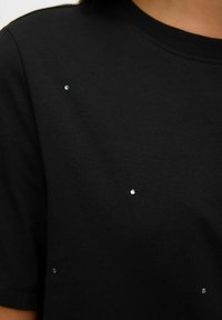 T-shirt in cotone nero con maniche corte, caratterizzata da strass luccicanti sparsi sul davanti. Tessuto morbido con collo tondo standard.