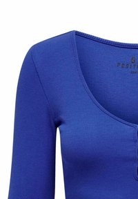 Top lungo a maniche, blu con costine, caratterizzato da un collo a barca e bottoni frontali, realizzato in tessuto elasticizzato per una vestibilità aderente.