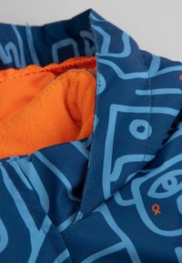 Granatowa kurtka z jasnoniebieskimi abstrakcyjnymi wzorami i pomarańczowym polarem wewnątrz, skupiając się na detalach kołnierza i materiału podszewki.