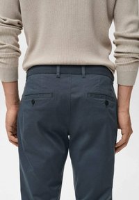 Tmavě šedé kalhoty z hladké látky s úzkým střihem, dvěma zadními kapsami s knoflíky a plochým předním dílem.