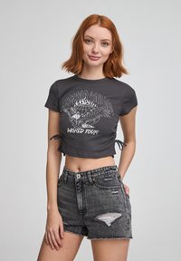 Cropped top grigio scuro con maniche corte, caratterizzato da una stampa grafica bianca, abbinato a shorts in denim neri strappati a vita alta.