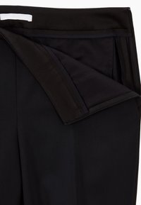 Mustat housut, joissa on piilotettu vetoketju ja vuorattu sisäosa. Sujuva pinta, räätälöity muotoilu ja sisäiset viimeistelyt parantavat käytettävyyttä.