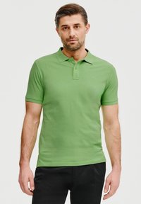 Zielona koszulka polo wykonana z bawełny, z krótkimi rękawami, klasycznym kołnierzykiem i listwą na trzy guziki. Jednolity kolor, gładka tekstura.