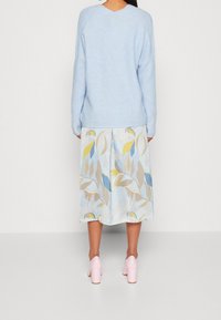 Jasnoniebieski sweter dzianinowy z dekoltem w kształcie v, w połączeniu z kwiecistą, midi spódnicą w pastelowych kolorach i różowymi butami na blokowym obcasie.