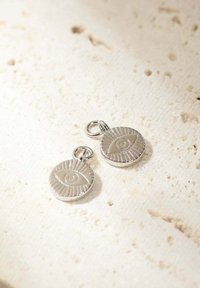 Pendente in argento con un design di occhio in rilievo, forma circolare con accenti rigati, posato su una superficie testurizzata.