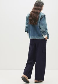 Giacca di jeans di colore azzurro chiaro, vestibilità rilassata, con chiusura a bottoni e maniche arrotolate; abbinata a pantaloni cargo a gamba larga di color blu navy con tasche laterali.