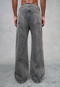 Jeans de denim grises de pierna ancha con pliegues visibles, dos bolsillos traseros y puños fruncidos. Presentan una textura única y sutiles acentos de metal.