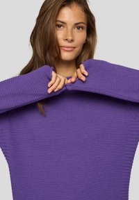 Lila gestrickter Pullover mit lockerer Passform, breiten Ärmeln und Rippstruktur. Der Stoff wirkt weich und leicht übergroß.