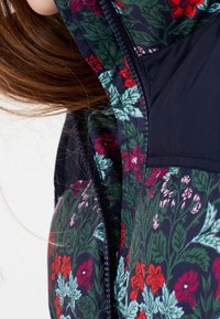 Blommig pufferjacka med marin bakgrund och röda och rosa blommor, gröna löv, hel dragkedja och en slät nylontextur.