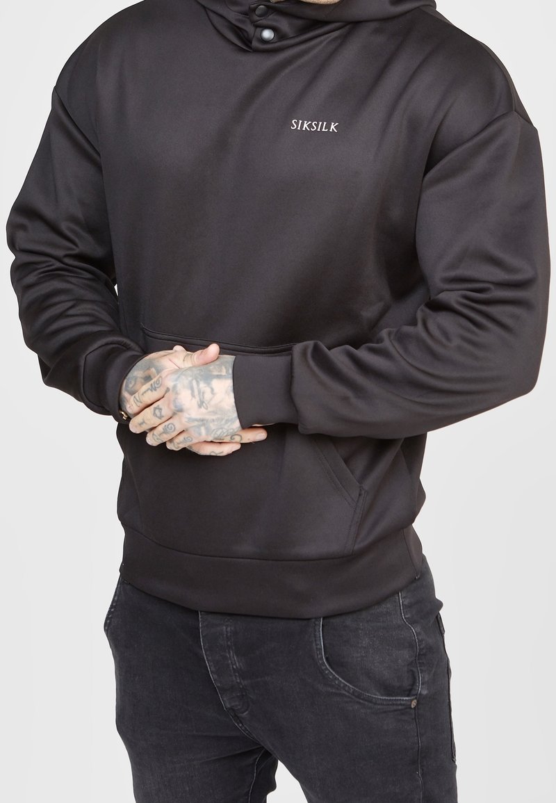Sudadera negra de tela suave con un bolsillo frontal, capucha ajustable con botones a presión y un pequeño logo en el pecho.