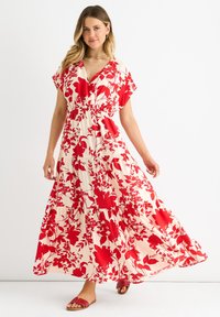 Maxi dress with a v-neck, short flutter sleeves, and an elastic waist. Features a red floral pattern on a cream background.