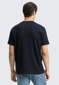 Granatowy t-shirt z krótkim rękawem i okrągłym dekoltem, wykonany z prążkowanej tkaniny, o luźnym kroju i gładkiej fakturze.