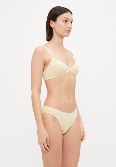 Light yellow bralette and matching bikini bottom made of soft fabric. Bralette features thin adjustable straps and a subtle scalloped edge.