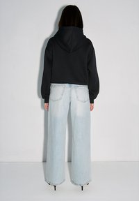 Czarna bluza z kapturem o luźnym kroju oraz jasnoniebieskie dżinsy z szerokimi nogawkami, charakteryzujące się wyblakłym wyglądem i subtelną fakturą. Czarne buty na wysokim obcasie.