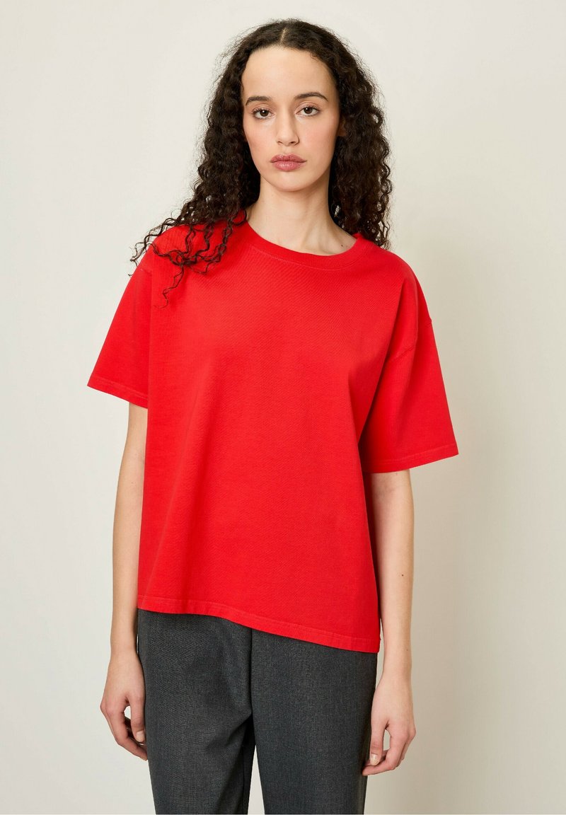 Raudona medvilninė marškinė su apvaliu kaklu ir trumpomis rankovėmis, pasižymi laisvu fasonu. Audinys turi glotnią tekstūrą su minimaliu dekoravimu.