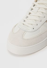 Białe trampki wykonane z połączenia gładkiej skóry i zamszu. Okrągły nos, płaskie sznurówki i teksturowana gumowa podeszwa. Subtelne detale przeszycia.