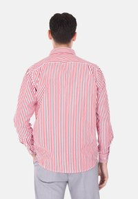 Camicia a maniche lunghe a righe rosse e bianche, con colletto classico e orlo curvo, realizzata in un tessuto morbido.