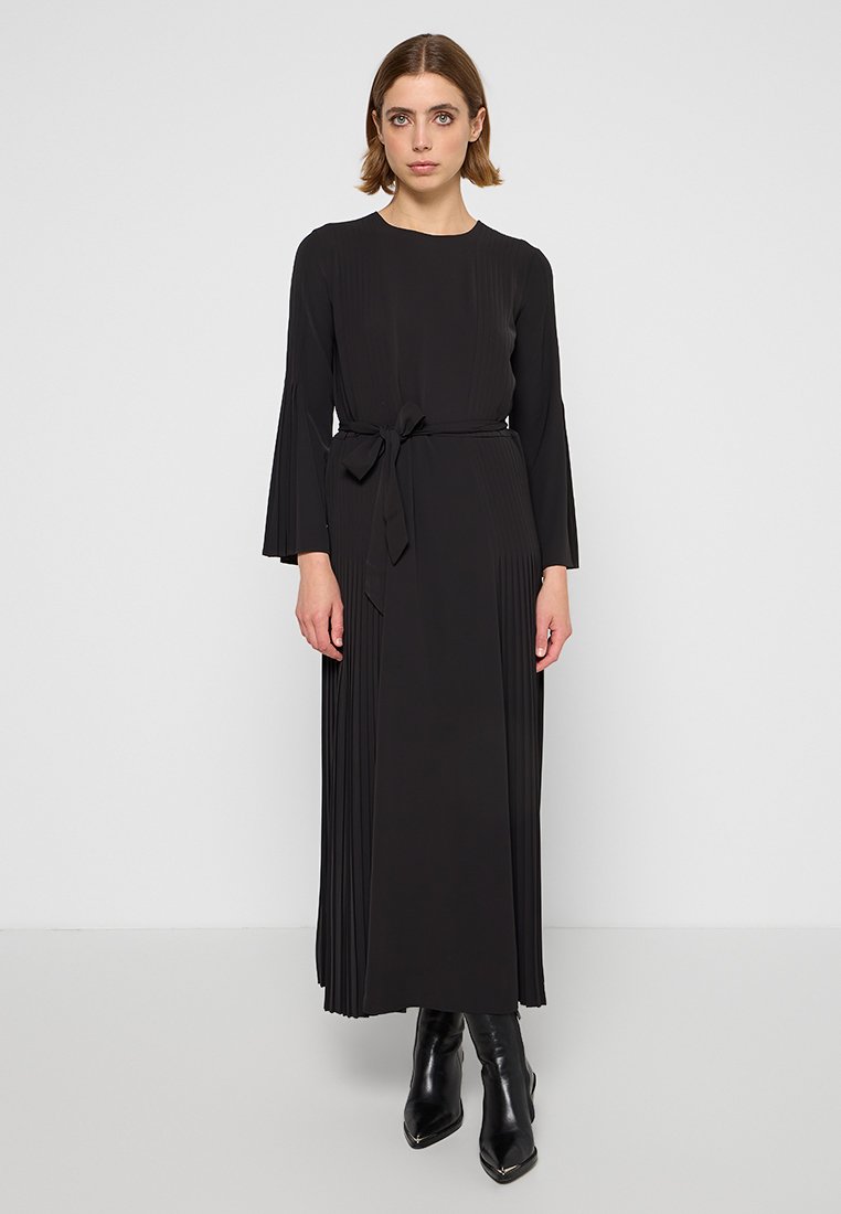 Abito nero plissettato con maniche lunghe, vita con cintura e texture morbida. Presenta un design lungo fino al pavimento e polsini delle maniche svasati.