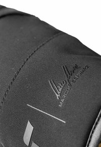 Schwarze Stofftasche mit glatter Textur, Nahtdetails und prägierter Unterschrift. Auffällige geometrische Akzente in einer kontrastierenden Farbe.