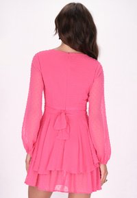 Rochie roz, cu buline, cu mâneci lungi, talie legată și fustă în straturi. Material moale, transparent, cu o textură netedă și un model subtil.